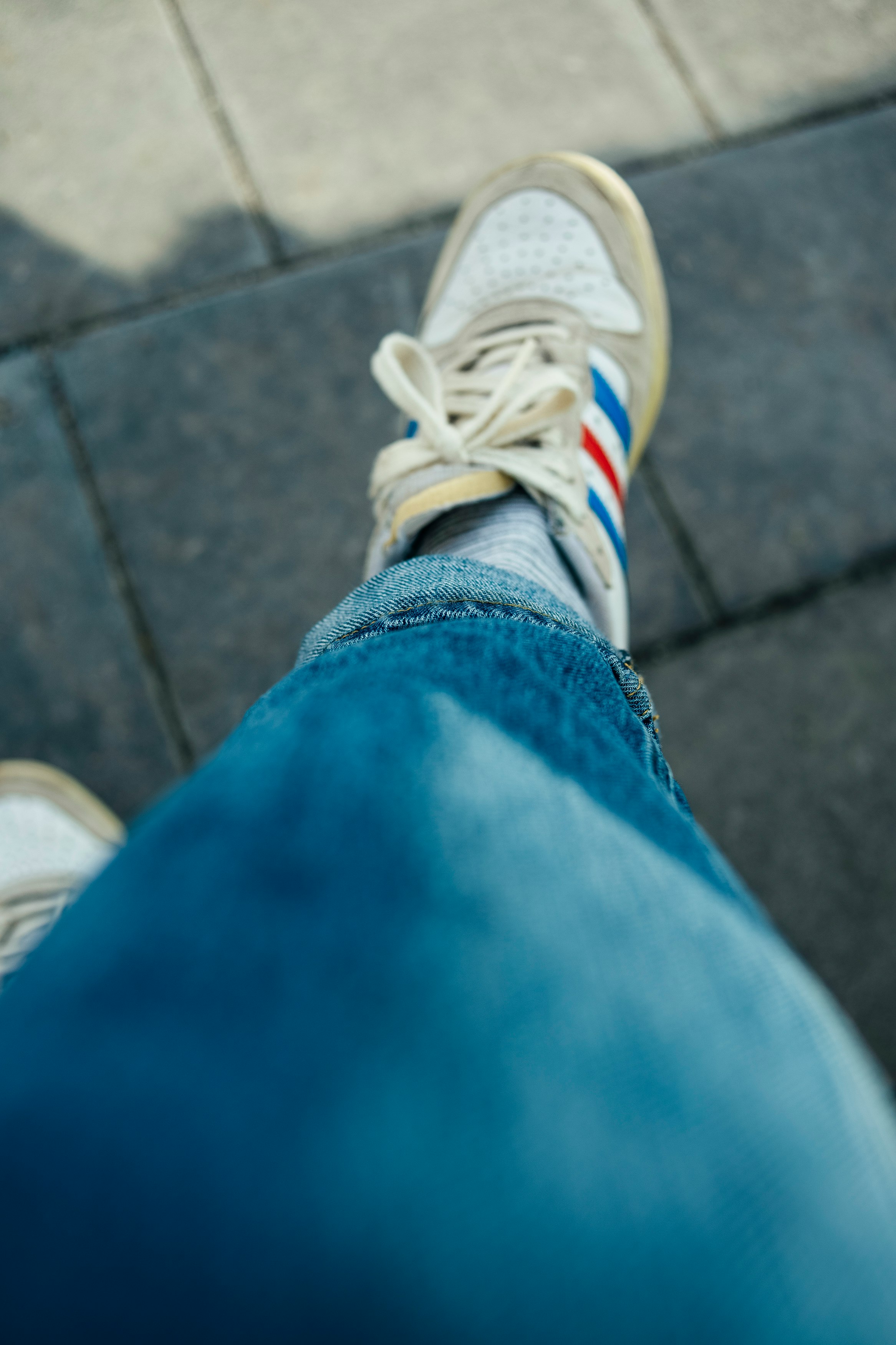 person in blue denim jeans wearing white and yellow adidas sneakers